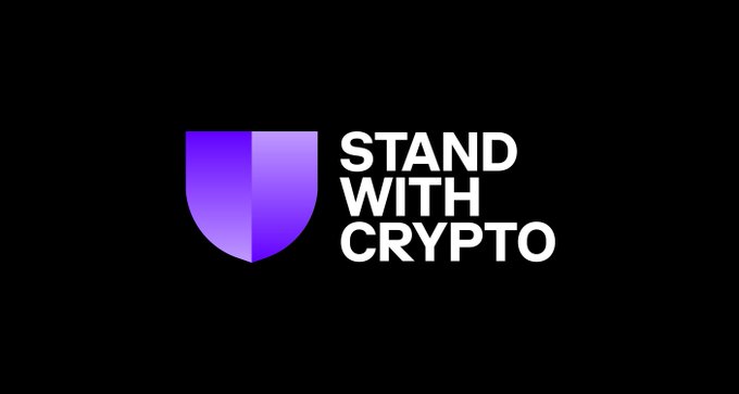 The image shows the "Stand With Crypto" logo, featuring a purple shield icon next to the bold white text on a black background. The logo represents the Coinbase-backed advocacy group referenced in the post, which has endorsed 32 pro-crypto candidates running in the midterm elections.