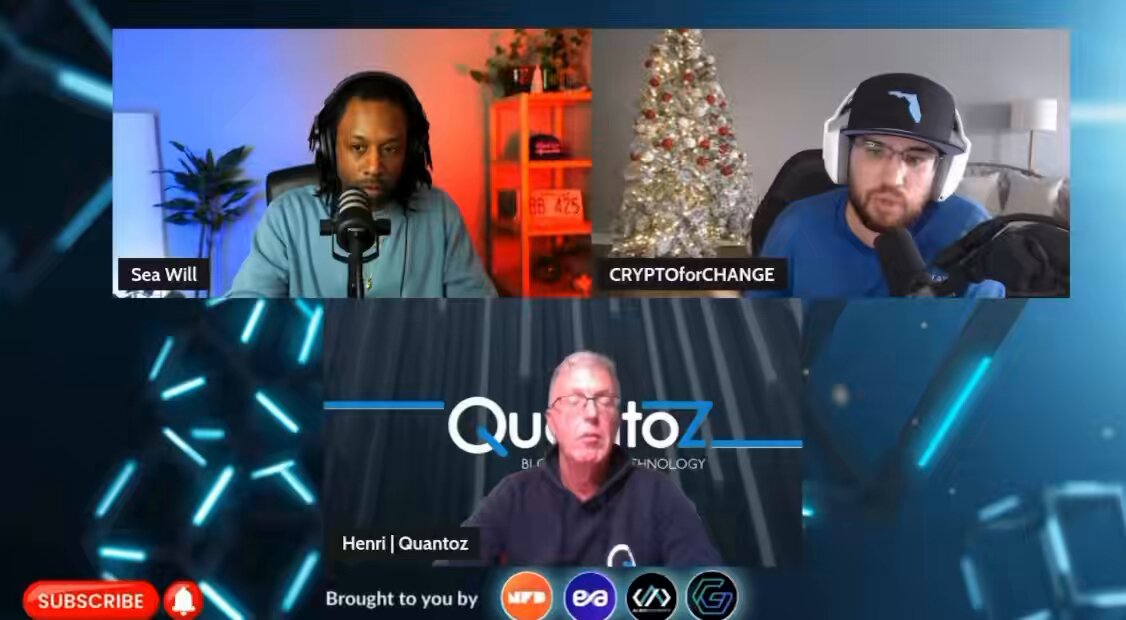 The image shows three men sitting at a table with microphones, appearing to be participating in an online podcast or radio show. The hosts are discussing the launch of a new cryptocurrency called @Quantoz. One man is wearing a blue shirt while another has on a black shirt. They are seated around a table that also holds a Christmas tree and a potted plant. The background features a blue screen with white text, which includes information about the launch of the new cryptocurrency and the names of its creators.