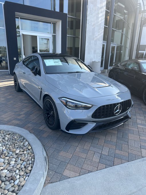 Photo of a gray Mercedes-Benz AMG coupe parked outside a dealership, with another dark car visible beside it.