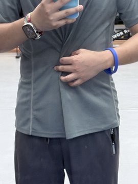 A person wearing a gray t-shirt and dark pants with a blue wristband, using both hands to stretch the fabric of their shirt outward.
