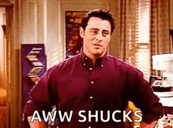 The image features a man wearing a red shirt, standing against a white wall with a poster hanging above him. Below his head, there's an arrow pointing towards him, and below that, the text "aww shucks" written in all capital letters. The background of the image is blurred, but it appears to be a room or a hallway.