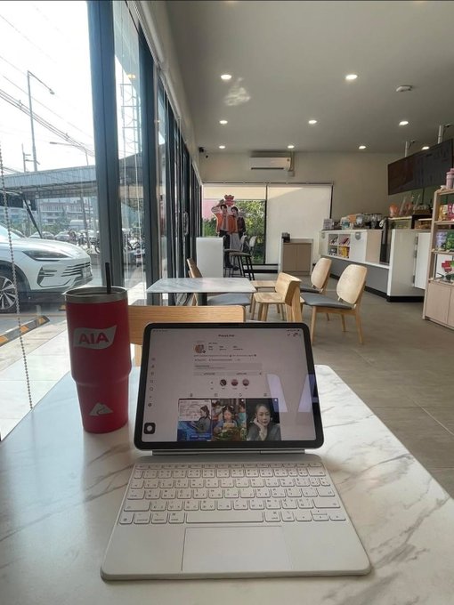 A tablet displaying a social media page sits on a marble table next to a red 'AIA' tumbler inside what appears to be a cafe or restaurant with large windows.