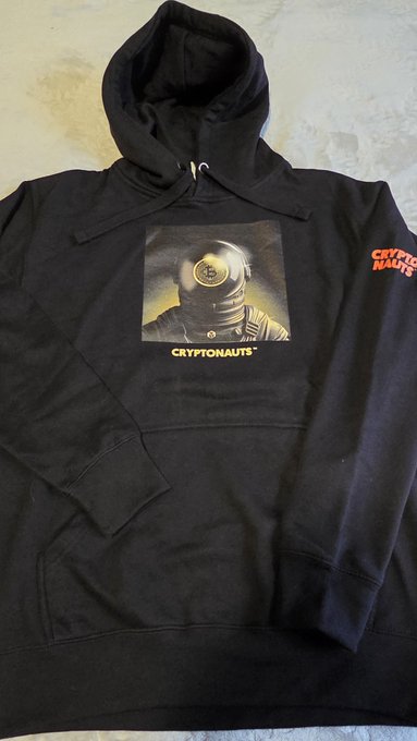 A black hoodie laid flat, featuring a printed graphic of an astronaut helmet and the text 'CRYPTONAUTS' on the chest, with 'CRYPTO NAUTS' printed on the right sleeve.