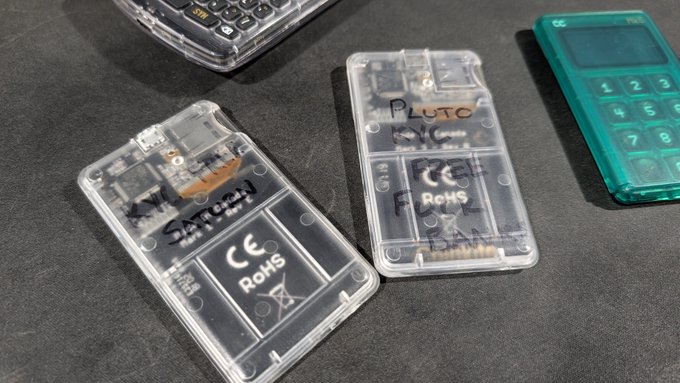 Two transparent calculators labeled "PLUTO" and "Pluto" rest on a dark surface alongside other calculators, with the post "RIP" referencing the character Pluto from "Your Lie in April," whose name is written on these clear devices as a memoriam.