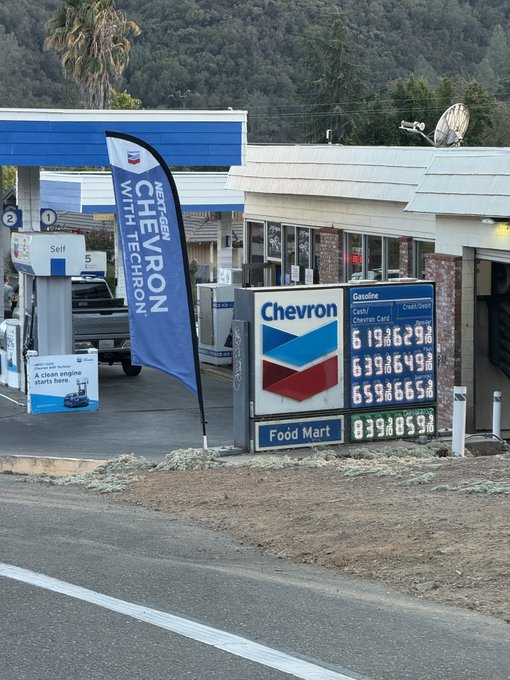 A Chevron gas station with its signature blue and red logo, featuring a 'NextGen Chevron with Techron' banner and a gas price sign displaying fuel costs.