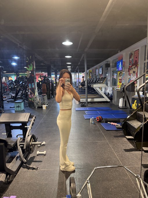 A woman in a cream-colored outfit takes a mirror selfie with her phone at a gym, surrounded by treadmills and workout equipment. The post expresses frustration over crypto performance—specifically mentioning $LUNA, $ben, and LUMA—while the image hints at her coping method: hitting the gym to reset.