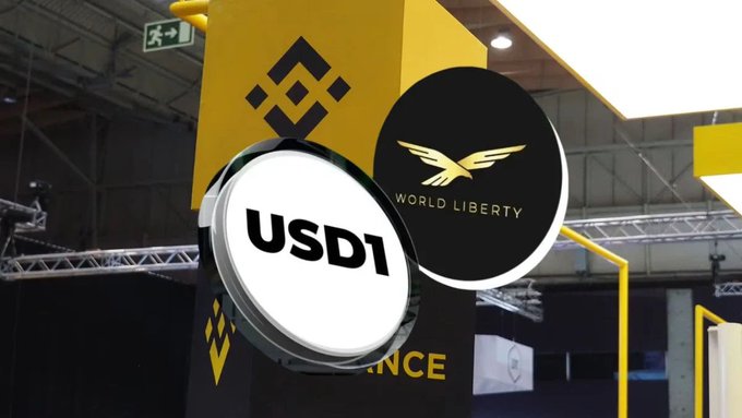 The image features a sign with two logos, one of which reads "USDC1" while the other says "World Liberty". The sign also has an arrow pointing towards the USDC1 logo. The background of the image shows a building or a large room, and there is a yellow sign in the scene as well.
