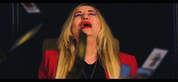 A woman with long blonde hair, wearing a red blazer and bold red lipstick, tilts her head back with her mouth open in an expression of shock or excitement, as paper money and what appears to be a tether (chain) fall around her. The dramatic, cinematic image humorously captures the post's theme of a thrilling, unpredictable "House of Tether" moment—mirroring either a dramatic movie scene or the intense emotions of watching the crypto market open.