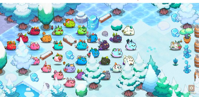 A snowy Axie Terrarium scene shows a large gathering of colorful Axie creatures assembled in an icy forest setting, presumably led by the elder snowman-like character "Alden the Wise" mentioned in the caption. The collection of frost-covered critters reflects the post's reference to Alden gathering his followers in the cold terrain.