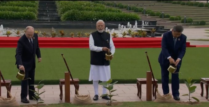 Three world leaders including what appears to be Vladimir Putin, Indian Prime Minister Narendra Modi, and another dignitary participate in a tree-planting ceremony, each holding a watering can next to a newly planted sapling at a formal garden venue.