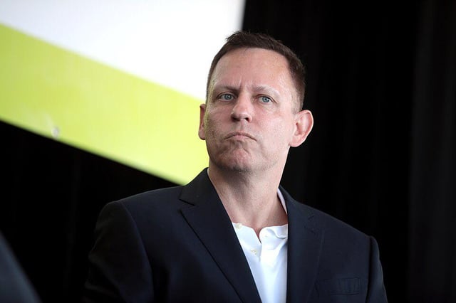 The image shows a man wearing a suit, standing against a black background with a green stripe running across it. He appears to be looking off into the distance or deep thoughtfully. The caption suggests that he might be thinking about something related to Bitcoin or the concept of Satoshi Nakamoto.