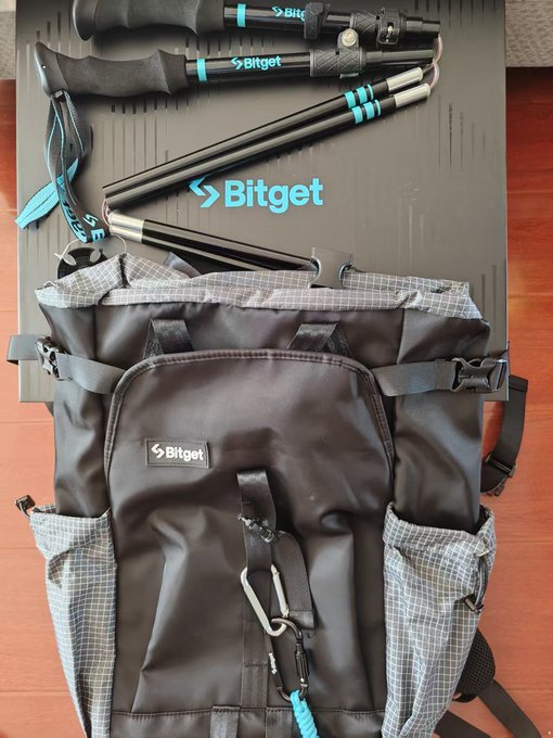 A black Bitget-branded backpack laid out with trekking poles and ski poles, all featuring the Bitget logo and teal accents.