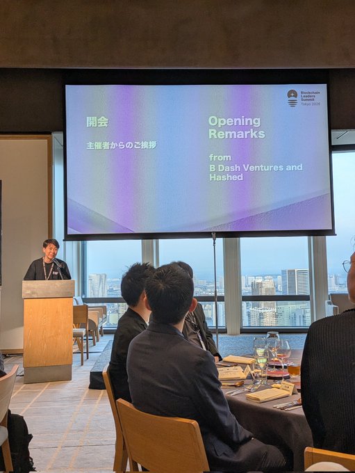 A speaker delivers opening remarks titled "Opening Remarks from B Dash Ventures and Hashed" at the Blockchain Leaders Summit Tokyo 2025, with attendees seated at a high-rise venue overlooking a city skyline. The image captures the formal conference setting that aligns with the post's mention of a fourth speaking engagement that day among impressive participants.