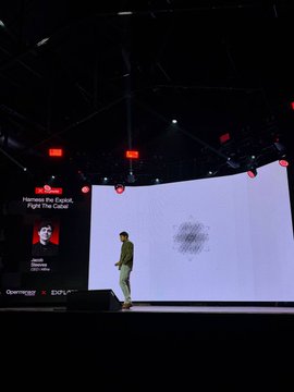 A speaker stands on a dimly lit conference stage with a large curved screen behind them, while a side panel displays "Harness the Capital, Light the Cosmos" alongside a speaker photo and the logos for Onemaxchain and ZKEX.