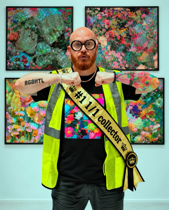 A bald man with a red beard, wearing a high-visibility vest and a sash that reads "#1 1/1 collector," poses in front of four colorful, abstract floral paintings.