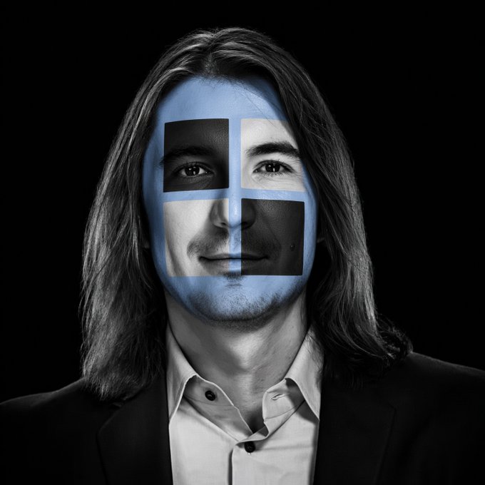 A portrait of a man with long hair wearing a suit, with the Finnish flag painted across his face.