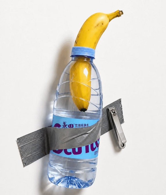 A clear plastic water bottle taped to a wall with a banana inserted through the cap, with a nail clipper taped to its side.
