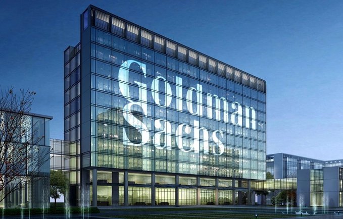 Goldman Sachs headquarters with "Goldman Sachs" displayed on the glass facade. The image illustrates the bank's recent call that a September Fed rate hike is unlikely, signaling potential relief for risk assets like crypto.