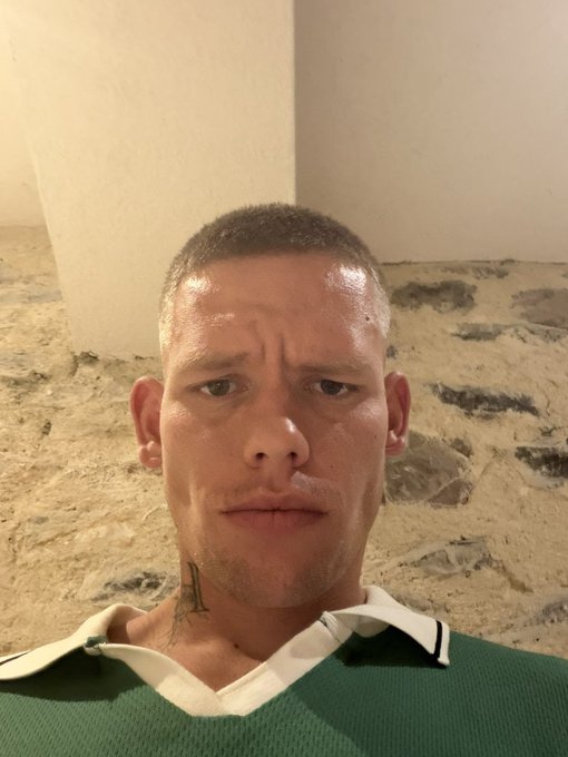 A sweaty, buzzcut man in a green and white collared shirt takes a serious selfie against a stone-walled background, his stern expression matching the confident energy of the caption "CHAD DOES WHAT CHAD WANT."