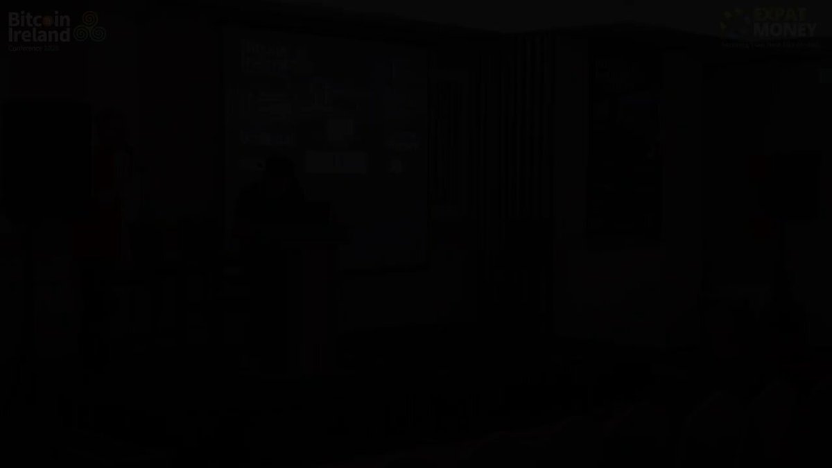 The image shows a person standing next to a black background with a window behind them. The person appears to be wearing a dark shirt or jacket, which contrasts with the overall darkness of the scene. The focus of the image seems to be on the person's presence and their relationship to the window in front of them.