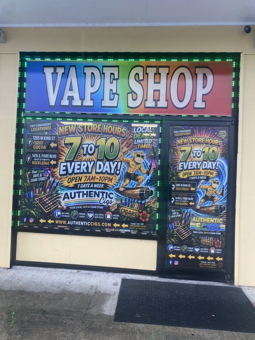 The storefront of a 'VAPE SHOP' with colorful illuminated window displays advertising 'NEW STORE HOURS 7 TO 10 EVERY DAY!', 'AUTHENTIC Cigs', 'TOUGH GUYS COCOA', and 'WE VAPE KNOWLEDGE'.