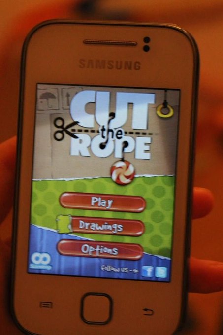 A Samsung smartphone displaying the main menu of the mobile game 'Cut the Rope' with options for Play, Drawings, and Options.