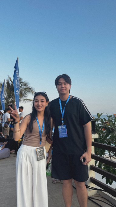 A young woman wearing a tan tank top and white pants poses with a peace sign next to a taller person in a black t-shirt and shorts, both wearing blue lanyards with "CRYPTO EXPO" badges. The image appears to capture a moment at a crypto conference, aligning with the post celebrating time spent with the "Crypto Queen" @roschamomile.