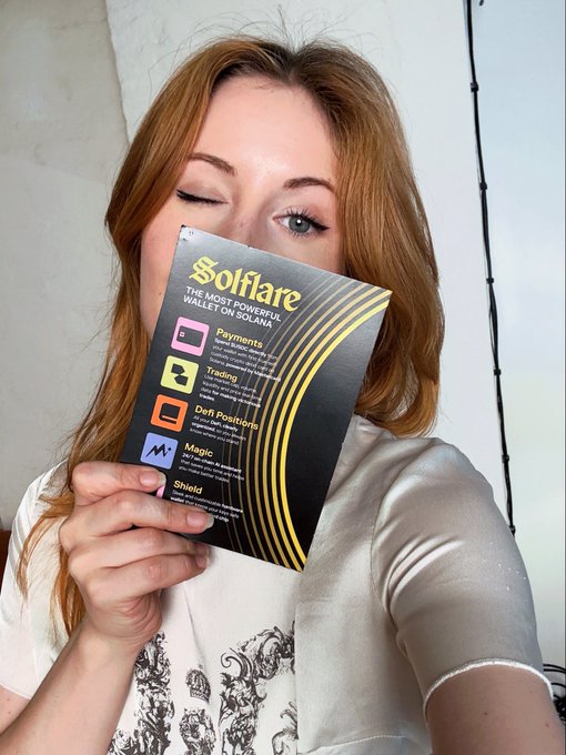 A woman with red hair holds a promotional card for 'Solflare - The Most Powerful Wallet on Solana' listing features like Payments, Trading, DeFi Positions, Magic, and Shield.
