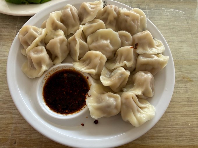 A plate of steamed dumplings served with a small bowl of spicy chili dipping sauce.