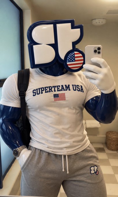 A mirror selfie of a person wearing a white 'SUPERTEAM USA' t-shirt and grey sweatpants, with their head replaced by an American flag graphic featuring the 'ST' logo.