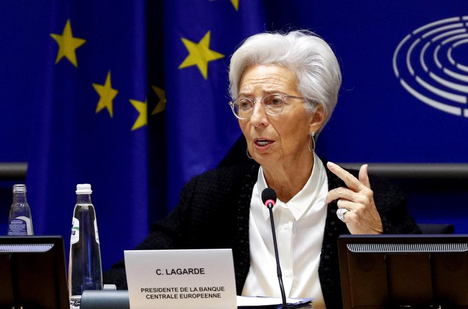 Christine Lagarde, identified by a nameplate reading 'C. LAGARDE, PRÉSIDENTE DE LA BANQUE CENTRALE EUROPÉENNE', speaks while gesturing at a podium with EU flags in the background.