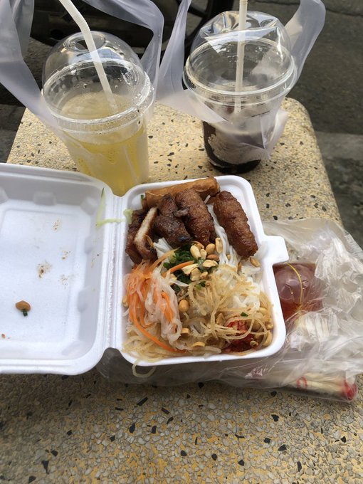 A takeout container holds a Vietnamese vermicelli noodle bowl topped with grilled pork, shredded carrots, bean sprouts, and peanuts, paired with a bright yellow drink and a dark iced beverage in plastic cups with straws. The casual street-food meal visually matches the post's caption of a morning combo of breakfast and coffee, captured as part of a relaxed check-in referencing @quipnetwork, #QUIP, #Quantum, and #Web3.