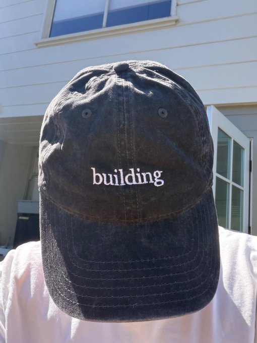 A weathered dark gray baseball cap with the word "building" embroidered in white sits in the foreground, fitting the "energy today and every day" caption by symbolizing the steady, ongoing effort of personal growth and development.
