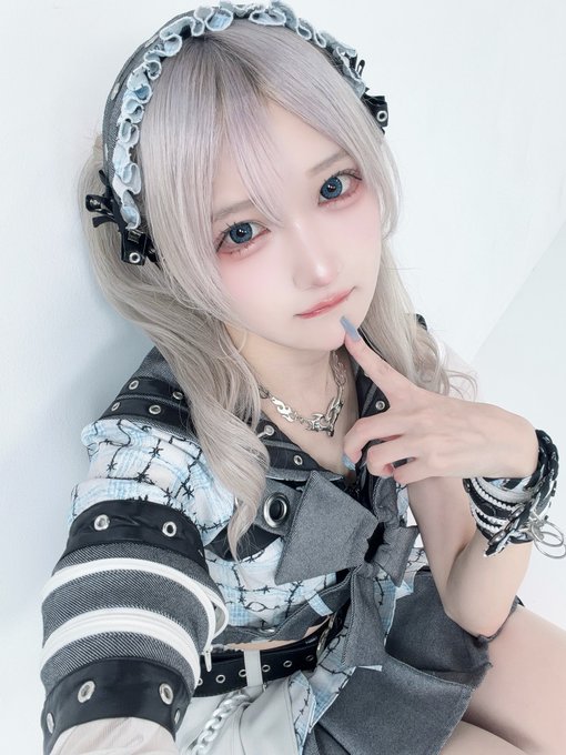 A person with long silver-blonde hair poses in a selfie, wearing a ruffled headband, chain necklace, and a black and white deconstructed outfit with grommet details, resting their finger near their chin. The caption "I am MEW (meow)." complements the image's soft, cat-like aesthetic with pastel tones and delicate styling.