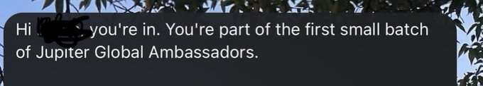 Digital display screen showing text reading 'Hi [name], you're in. You're part of the first small batch of Jupiter Global Ambassadors.' with tree foliage partially obscuring the view.