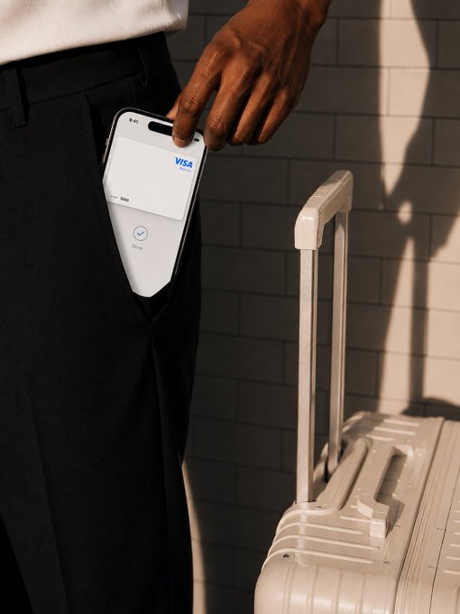 A person pulls out a smartphone from their pocket displaying a Visa digital card setup screen, standing next to a beige suitcase against a tiled wall, perfectly capturing the convenience of tapping into 150M Visa merchants worldwide.