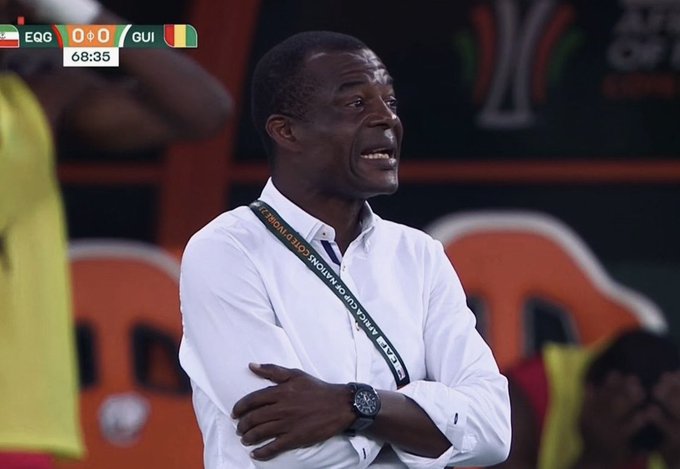 A coach with a "TOTAL ENERGIES AFRICA CUP OF NATIONS" lanyard grimaces with arms crossed during a match between EQG and GUI tied at 0-0 in the 69th minute (68:35). The image captures a tense, frustrated sideline moment that humorously mirrors the stress of high-leverage trading portrayed in the accompanying post.