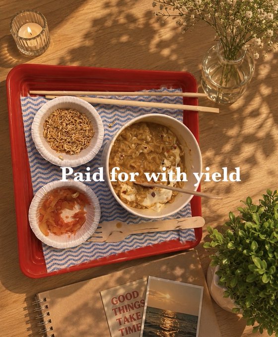 An overhead shot of a red tray holding a meal of instant noodles, kimchi, and ramen, with the overlaid text "Paid for with yield."