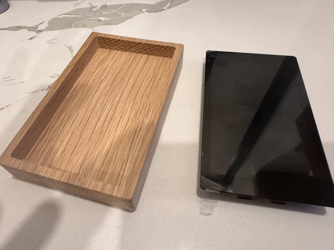 A carved wooden tray sits on a marble countertop next to a black tablet or monitor with USB-C ports visible along its bottom edge.