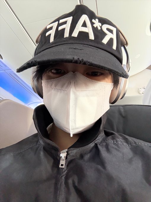 A selfie of a young man wearing a black cap with 'RAFF' text in mirrored lettering, a white face mask, and over-ear headphones.