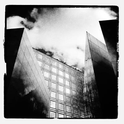 A dramatic black and white low-angle photograph of modern glass skyscrapers reaching toward a cloudy sky.