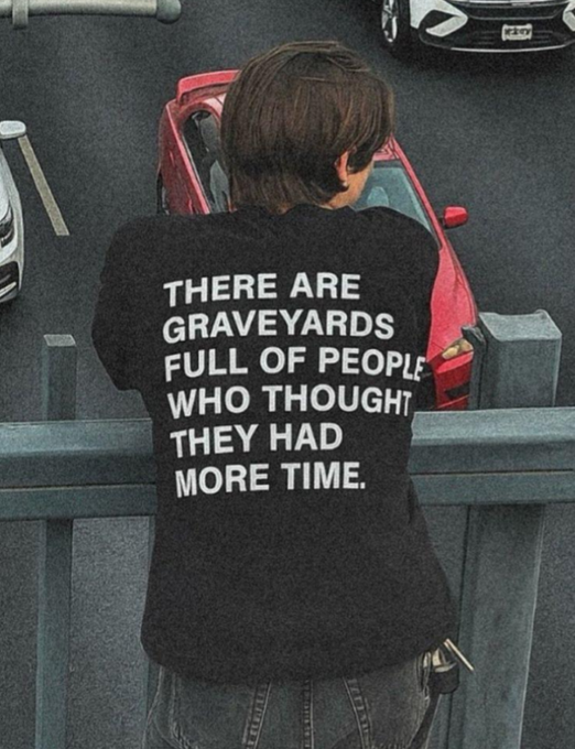 A person seen from behind wears a black sweater with the bold white text 'THERE ARE GRAVEYARDS FULL OF PEOPLE WHO THOUGHT THEY HAD MORE TIME.'