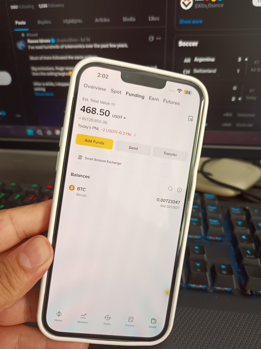 A smartphone displaying a crypto trading app with an estimated total value of 468.50 USDT and a BTC balance of 0.00723347, held in front of a computer monitor showing a Kaito.finance interface.