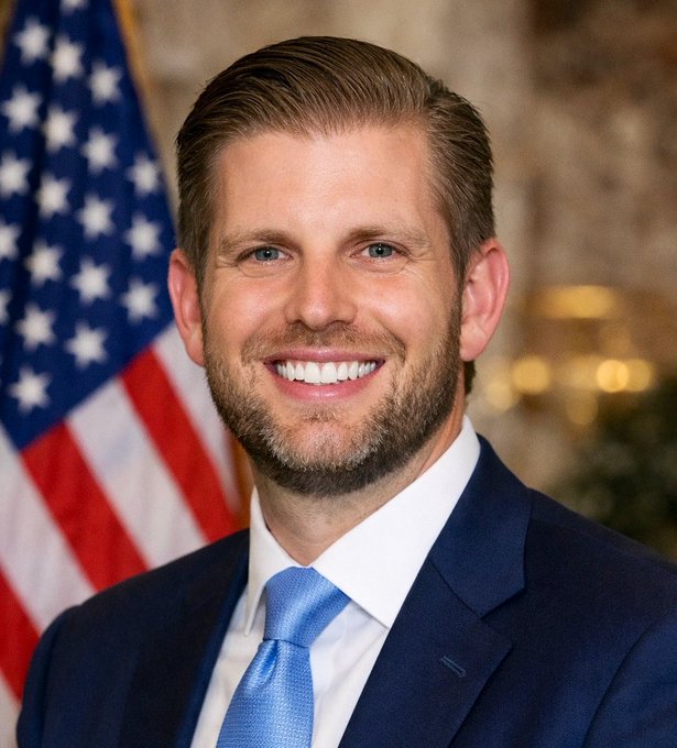 The image shows Eric Trump, identifiable by his resemblance to his father and the formal portrait style, smiling in a dark suit with a blue tie in front of an American flag, accompanying his bold prediction that Bitcoin will reach $1,000,000.