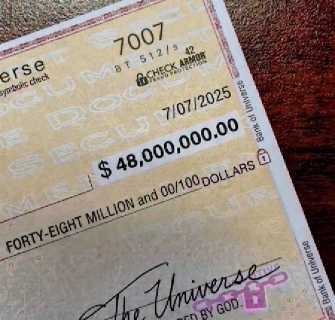 A close-up of a large novelty check from 'The Universe' made out for $48,000,000.00, dated 7/07/2025, with check number 7007 and a 'Check Armor' fraud protection stamp.