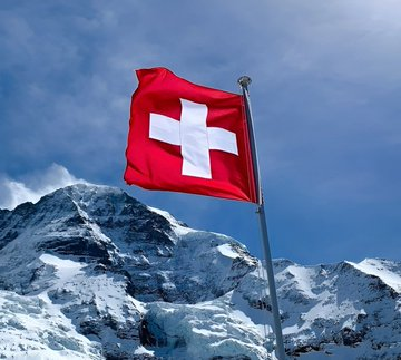 The Swiss flag waves majestically over snow-capped Alps, symbolizing Switzerland as the Swiss National Bank reveals a 736,300-share stake in Bitcoin treasury company Strategy, valued at approximately $72.4 million.