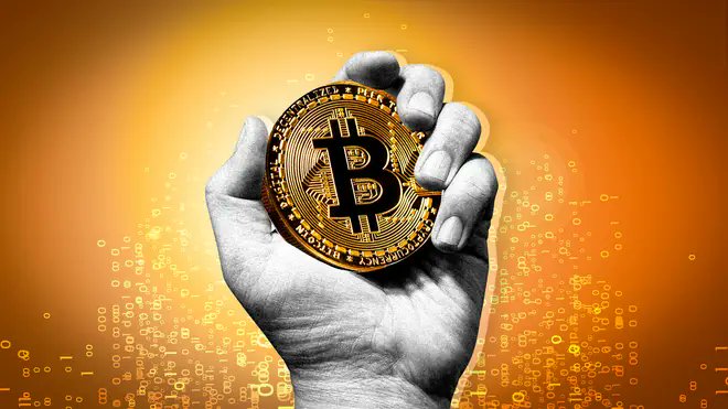 A black and white image of a hand holding a gold Bitcoin coin against an orange background featuring falling binary code.