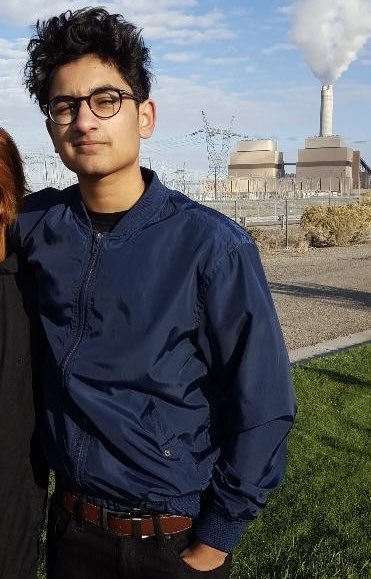 A young man wearing glasses and a navy bomber jacket stands outdoors with what appears to be a nuclear power plant cooling tower emitting steam in the background, alongside another partially visible person. The post celebrates crypto trader "FRANKDEGODS" for having the largest realized PNL on the FOMO platform at $3.29M, dwarfing second-place FROGMAN's $1.28M, though the image itself doesn't show any trading data or text.