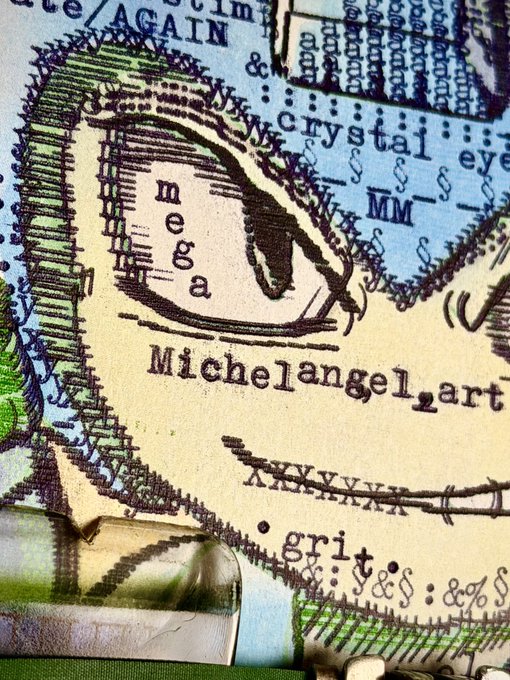 A close-up photograph of an intricate artwork featuring a face with the words "mega" and "Michelangelo_art" written below it, along with various sections labeled "AGAIN," "crystal eye," and "MM."