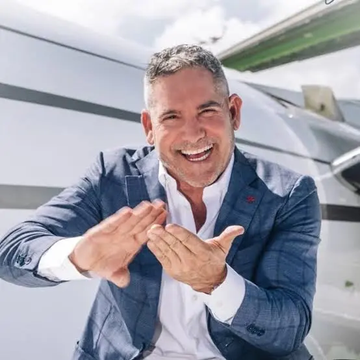 A smiling man in a blue blazer, identified as Grant Cardone based on the accompanying post, gestures enthusiastically while standing in front of a private jet, projecting an image of success that aligns with his announcement of Cardone Capital purchasing an additional 350 $BTC worth approximately $22.3 million.